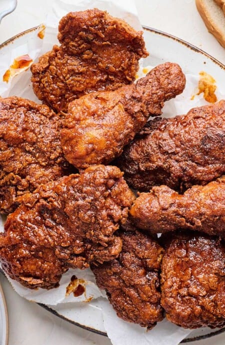 A platter of Nashville hot chicken on the table with a little bowl of pickles and slices of white bread.