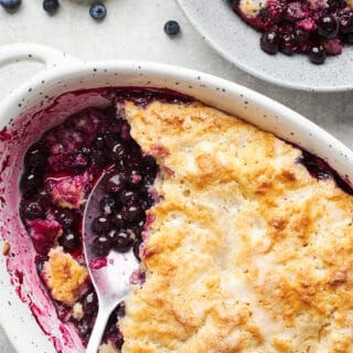 A serving spoon in a baking dish of fresh blueberry cobbler.