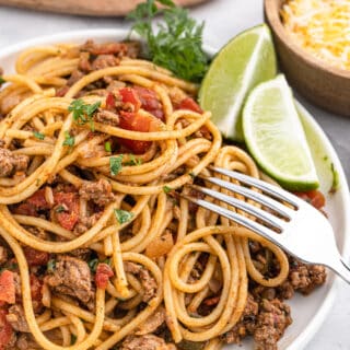 Completed dish of taco spaghetti garnished with lime wedges.
