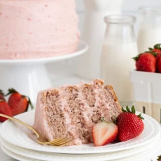 A slice of strawberry layer cake on white plates with a full cake in the background